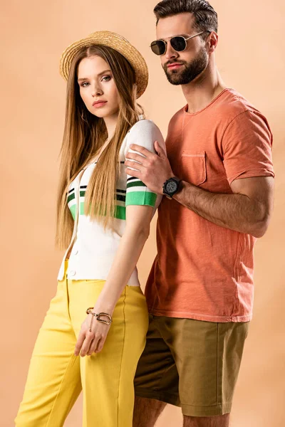 Hermosa joven pareja elegante posando en ropa de verano, sombrero de paja y gafas de sol en beige - foto de stock