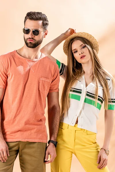 Beautiful couple posing in summer clothes, straw hat and sunglasses on beige — Stock Photo