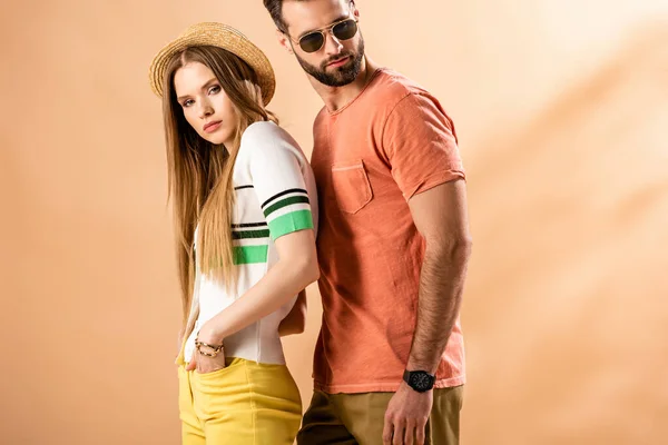 Красивая стильная пара, позирующая в летней одежде, соломенной шляпе и солнечных очках на бежевом — стоковое фото