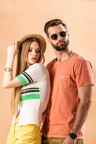 Hermosa pareja de moda posando en ropa de verano, sombrero de paja y gafas de sol en beige - foto de stock
