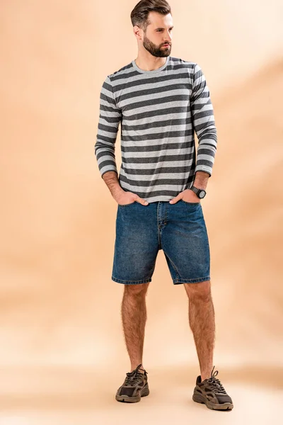 Stylischer bärtiger Mann posiert in gestreiftem Sweatshirt auf beige — Stockfoto