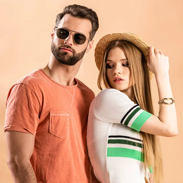 Beautiful fashionable couple posing in summer clothes, straw hat and sunglasses on beige — Stock Photo