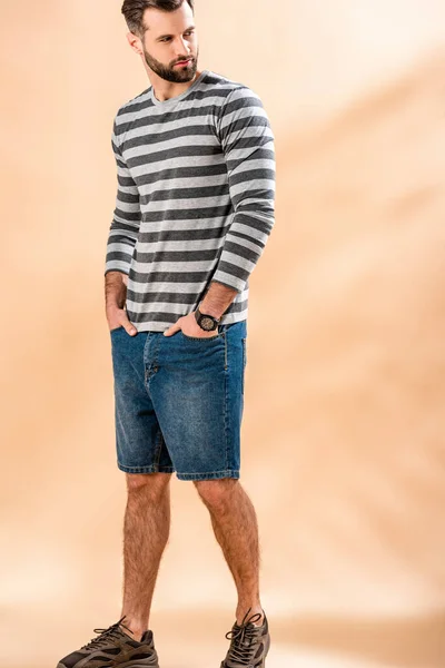 Красивий бородатий чоловік позує в смугастій сорочці на бежевому — стокове фото