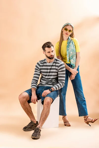 Fashionable couple posing in summer clothes on white cube on beige — Stock Photo
