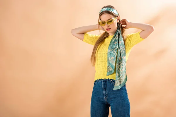 Bella ragazza alla moda in posa in jeans, t-shirt gialla, occhiali da sole e sciarpa di seta su beige — Foto stock