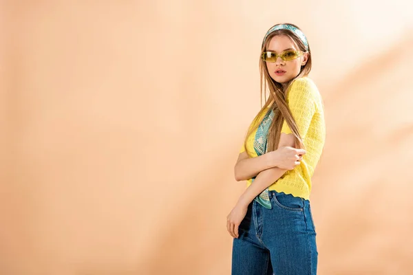 Красивая девушка позирует в джинсах, желтой футболке, солнечных очках и шелковом шарфе на бежевом — стоковое фото