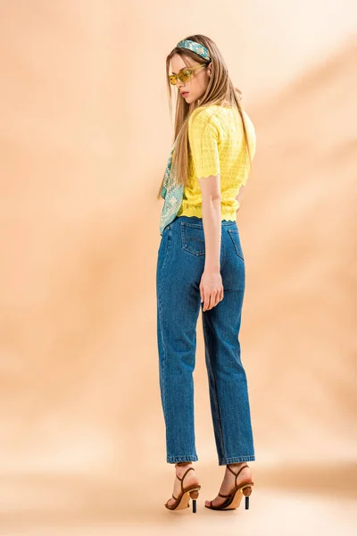 Menina na moda posando em jeans, camiseta amarela, óculos de sol e cachecol de seda no bege — Fotografia de Stock