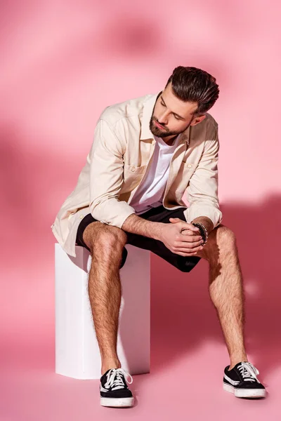 Stylischer bärtiger Mann posiert in Sommerhemd und Shorts auf weißem Würfel auf rosa — Stockfoto