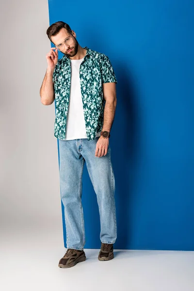 Бородатый стильный мужчина позирует в летней одежде и солнцезащитных очках на сером и синем — стоковое фото