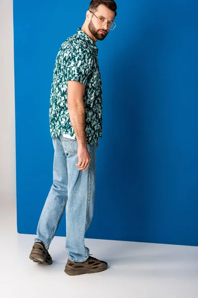 Hombre barbudo elegante posando en ropa de verano y gafas de sol en gris y azul - foto de stock