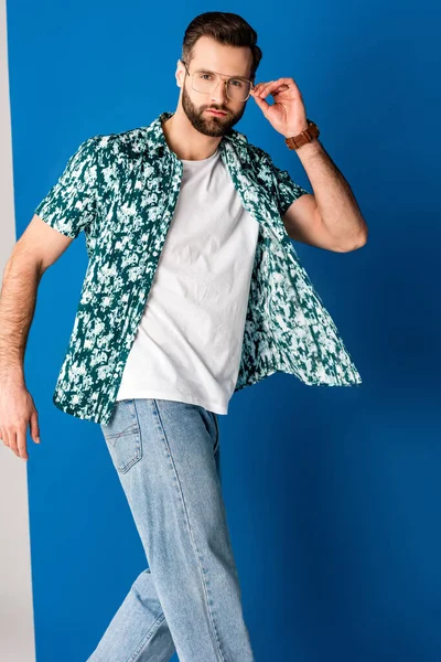 Handsome fashionable man posing in summer clothes and sunglasses on grey and blue — Stock Photo