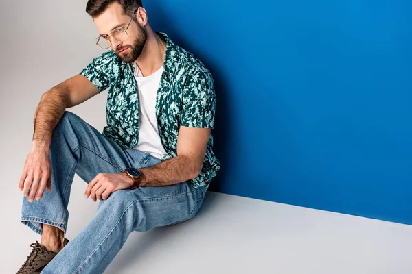 Hombre barbudo guapo posando en ropa de verano y gafas de sol en gris y azul - foto de stock