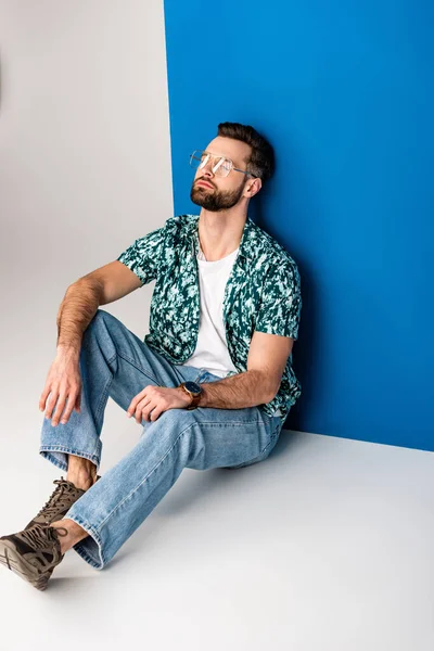 Красивый мужчина позирует в летней одежде и солнечных очках на сером и синем — стоковое фото