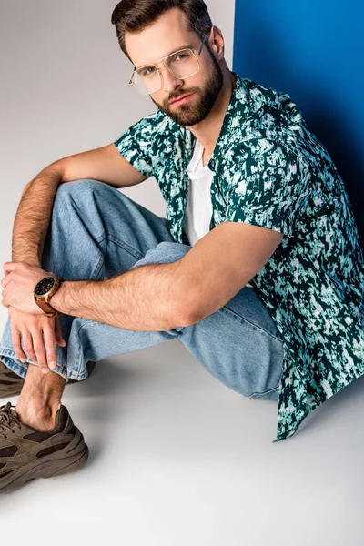 Stylish young man posing in summer clothes and sunglasses on grey and blue — Stock Photo