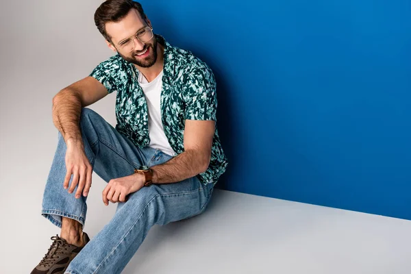 Hombre barbudo elegante posando en ropa de verano y gafas de sol en gris y azul - foto de stock