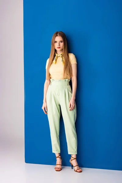 Fashionable girl posing in green summer trousers and heeled sandals on grey and blue — Stock Photo