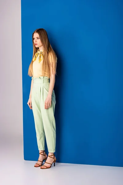 Stylish girl posing in green summer trousers and heeled sandals on grey and blue — Stock Photo