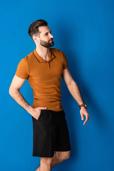 Stylish positive man posing in shorts and brown polo on blue — Stock Photo