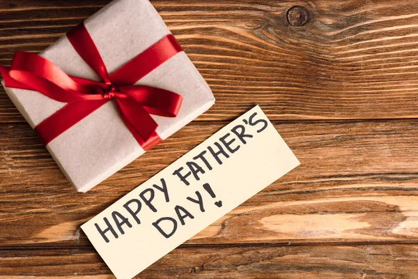 Top view of greeting card with lettering happy fathers day and pink gift box with red bow on wooden background — Stock Photo