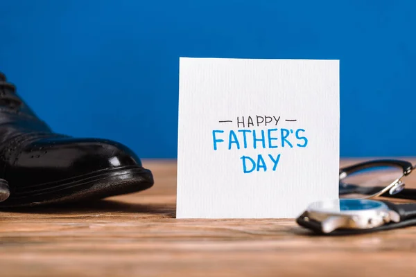 Selektiver Fokus der Grußkarte mit Schriftzug Happy Vatertag, Herrenschuhe, Armbanduhr und Brille isoliert auf blau — Stockfoto
