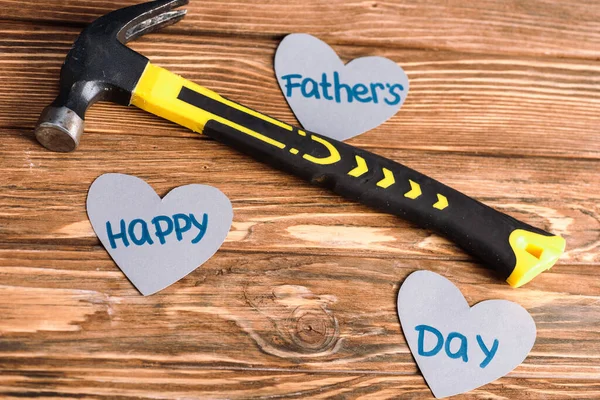 Vista de alto ángulo de martillo y papel cortado corazones grises con palabras feliz día de los padres sobre fondo de madera — Stock Photo