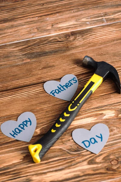 Vista de alto ángulo de martillo y papel corazones grises con palabras feliz día de los padres sobre fondo de madera - foto de stock