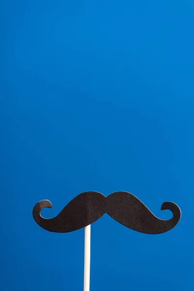 Decorative black paper crafted fake mustache on white stick isolated on blue — Stock Photo