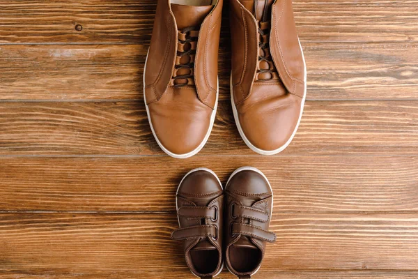 Pour voir des chaussures décontractées marron pour hommes et enfants sur fond de bois texturé, concept de fête des pères — Photo de stock