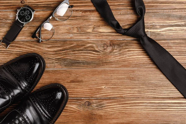 Vista superior de zapatos negros para hombre, corbata, reloj de pulsera y gafas sobre fondo de madera - foto de stock