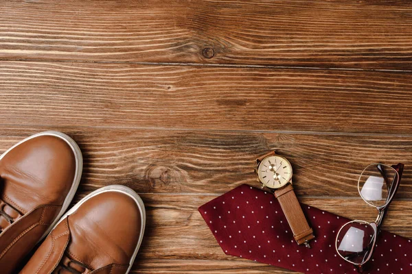 Draufsicht auf Herren braune Freizeitschuhe, gepunktete rote Krawatte, Armbanduhr und Brille auf Holzgrund — Stockfoto