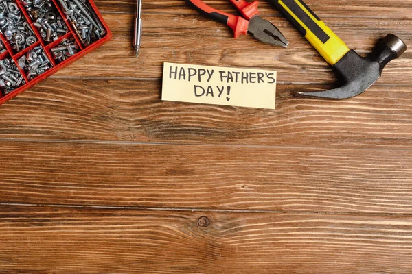 Top view of greeting card with handwritten lettering happy fathers day, hammer, pliers, screwdriver, nuts and bolts on wooden background — Stock Photo