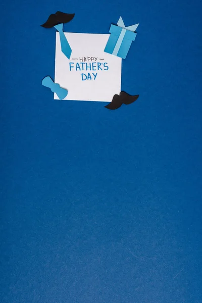 Vista superior de la tarjeta de felicitación con letras feliz día de los padres y artesanía de papel elementos decorativos creativos sobre fondo azul - foto de stock
