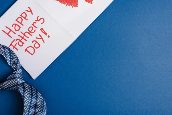 Top view of mens tie and greeting card with lettering happy fathers day on blue background — Stock Photo