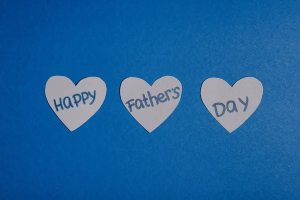 Vista superior de los corazones hechos a mano de papel gris con letras feliz día de los padres sobre fondo azul - foto de stock