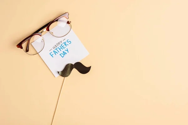 Top view of mens glasses, decorative paper mustache and greeting card with lettering happy fathers day on beige background — Stock Photo