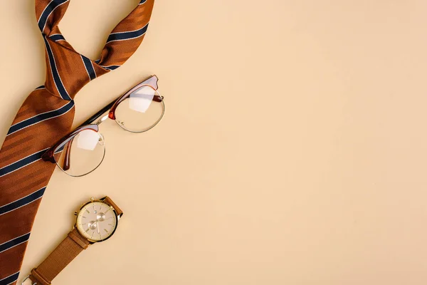 Верхний вид мужской полосатый галстук, наручные часы и очки на бежевом фоне — стоковое фото