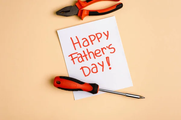 Top view of screwdriver, pliers and greeting card with lettering happy fathers day on beige background — Stock Photo