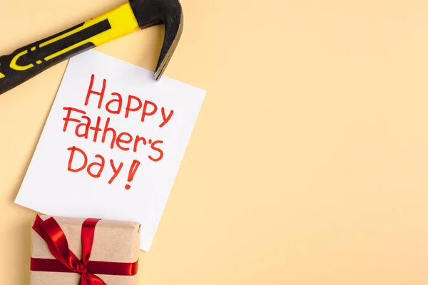 Vista superior de martillo, caja de regalo y tarjeta de felicitación con letras feliz día de los padres sobre fondo beige — Stock Photo