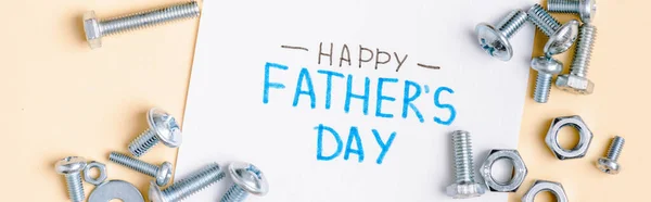 Panoramic shot of nuts and bolts and greeting card with lettering happy fathers day on beige background — Stock Photo