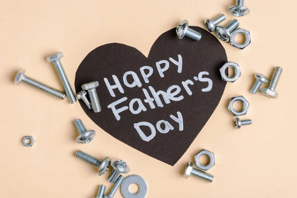 Vista superior de tuercas de metal y pernos y tarjeta de felicitación negro con letras feliz día de los padres sobre fondo beige - foto de stock