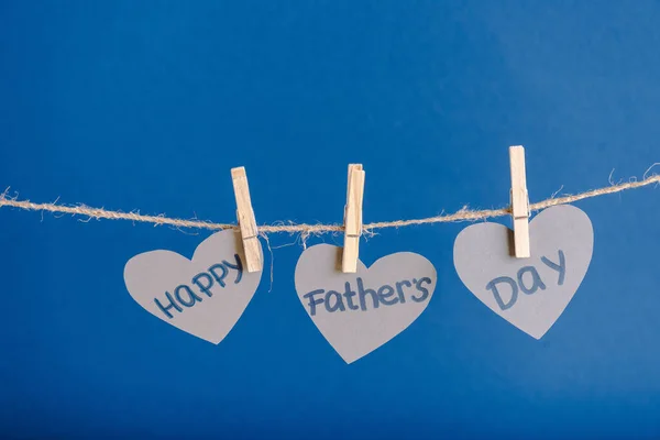 Tarjetas de felicitación en forma de corazón grises colgando de una cuerda con pinzas de ropa aisladas en azul - foto de stock