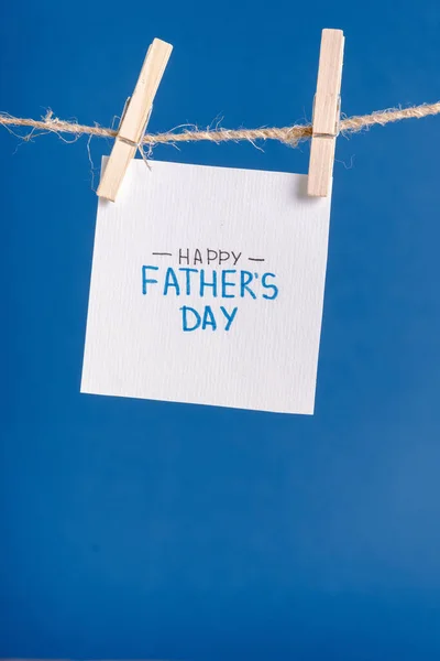 White paper with handwritten lettering happy fathers day hanging on rope with clothespins isolated on blue — Stock Photo