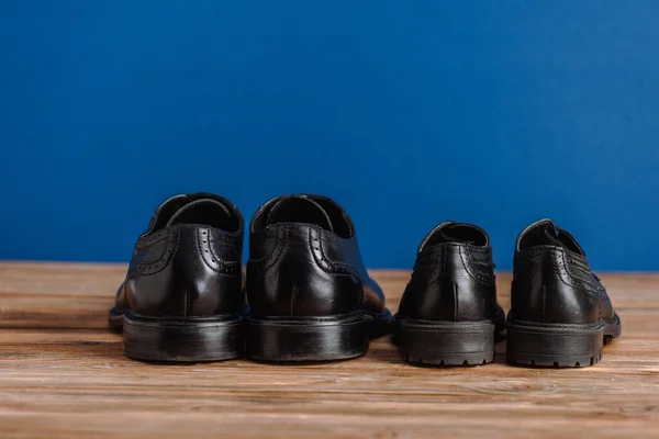 Negro para hombre y niños zapatos clásicos en la superficie de madera aislado en azul, padre concepto de día - foto de stock