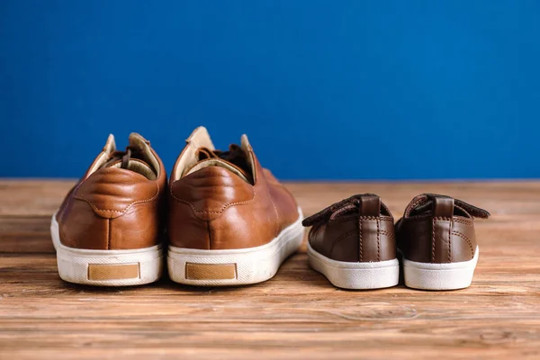 Chaussures décontractées pour hommes et enfants marron sur surface en bois texturée isolée sur bleu, concept de fête des pères — Photo de stock