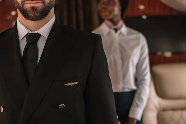 Cropped view of pilot and african american stewardess in private plane — Stock Photo