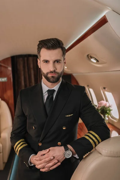 Piloto guapo y seguro de sí mismo mirando a la cámara mientras está de pie en el avión — Stock Photo