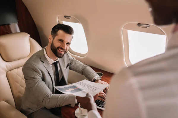 Selektiver Fokus eines gutaussehenden Geschäftsmannes, der auf eine afrikanisch-amerikanische Stewardess blickt, die ihm Zeitung schenkt — Stockfoto