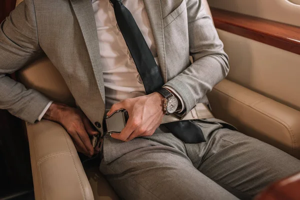 Cropped view of businessman fastening safety belt while sitting in private jet — Stock Photo