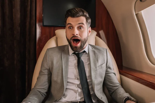 Sorprendido hombre de negocios con la boca abierta y los ojos abiertos sentados en avión privado - foto de stock