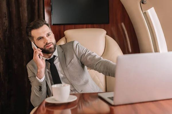 Selective focus of handsome businessman talking on smartphone in private plane — Stock Photo